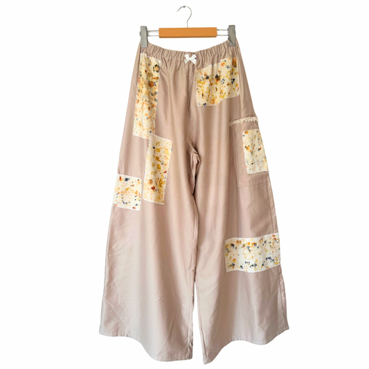 Beige pants with floral patchwork on a hanger against a white background.
Naturally dyed with homegrown flowers.