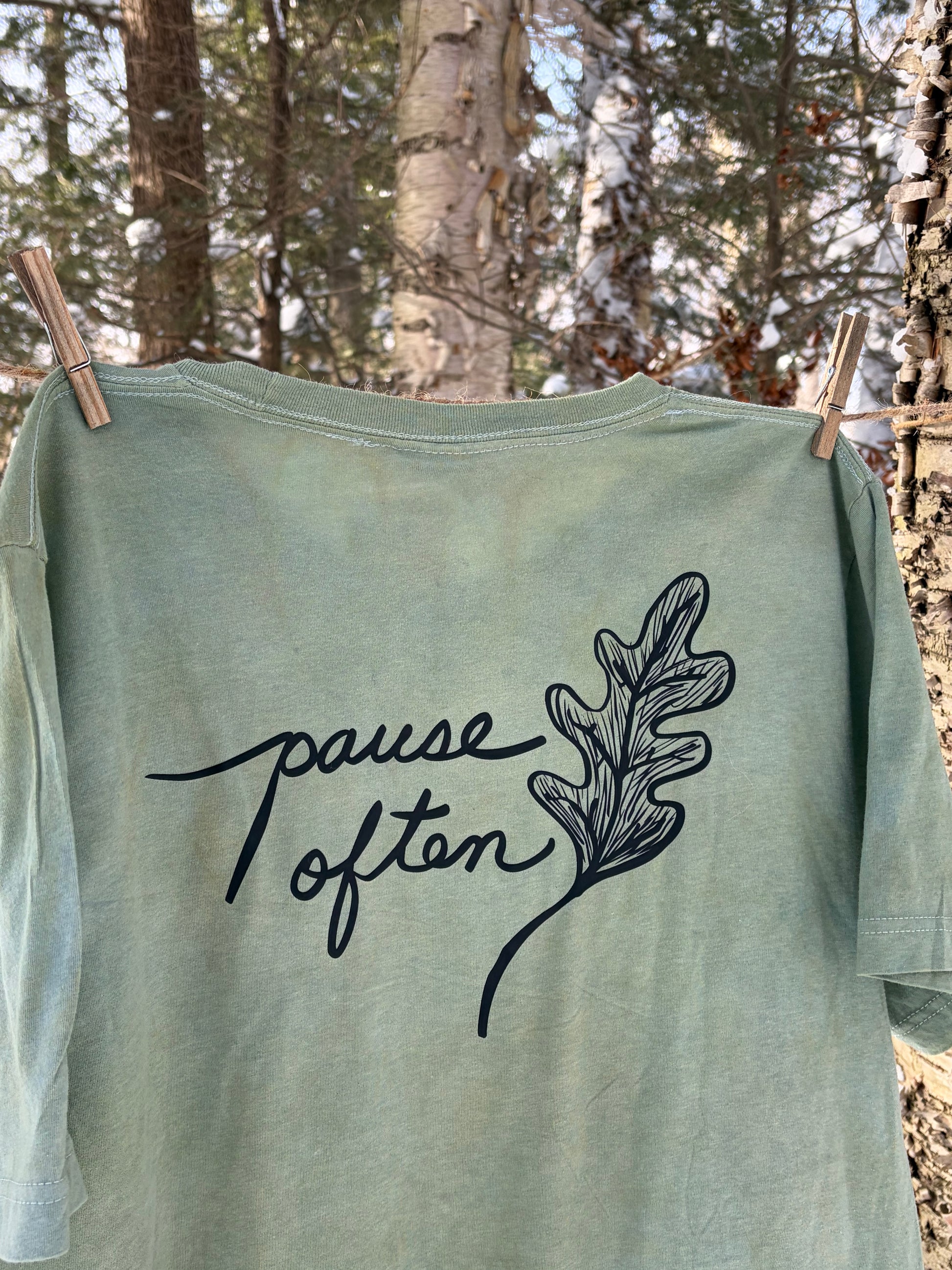 Green tee with Pause Often and oak leaf design hanging in the trees. Plant Dyed.