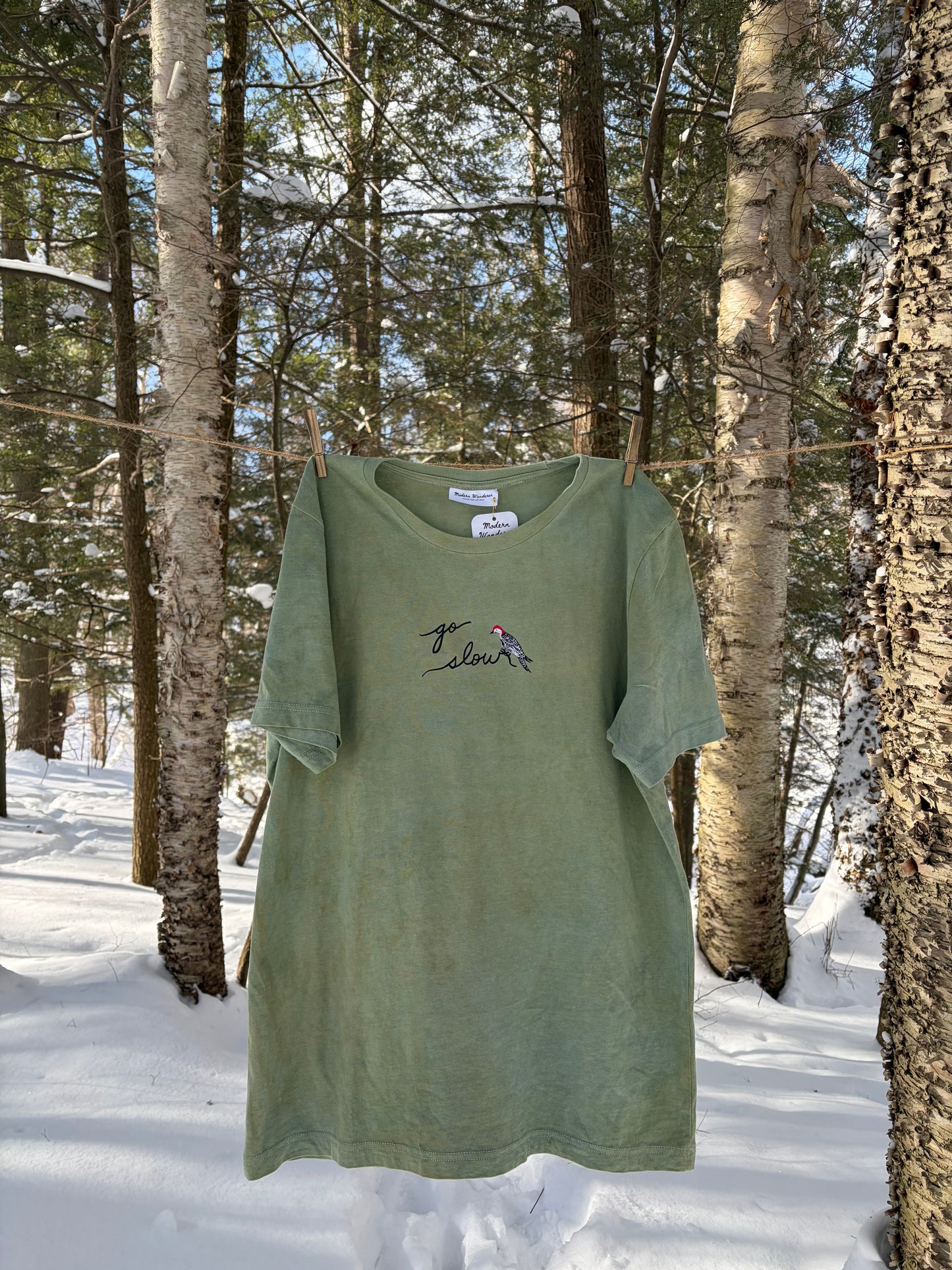Green t-shirt with embroidery in a snowy forest setting